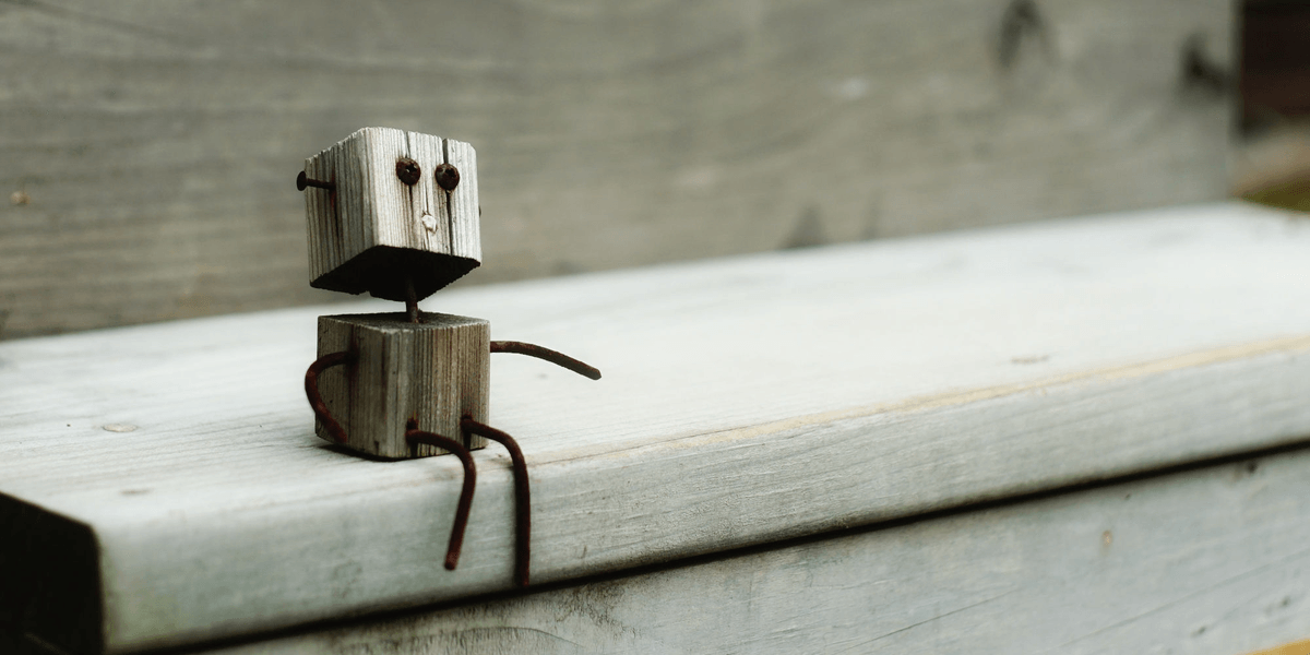 A small handmade wooden robot figurine sitting on a weathered wooden plank.
